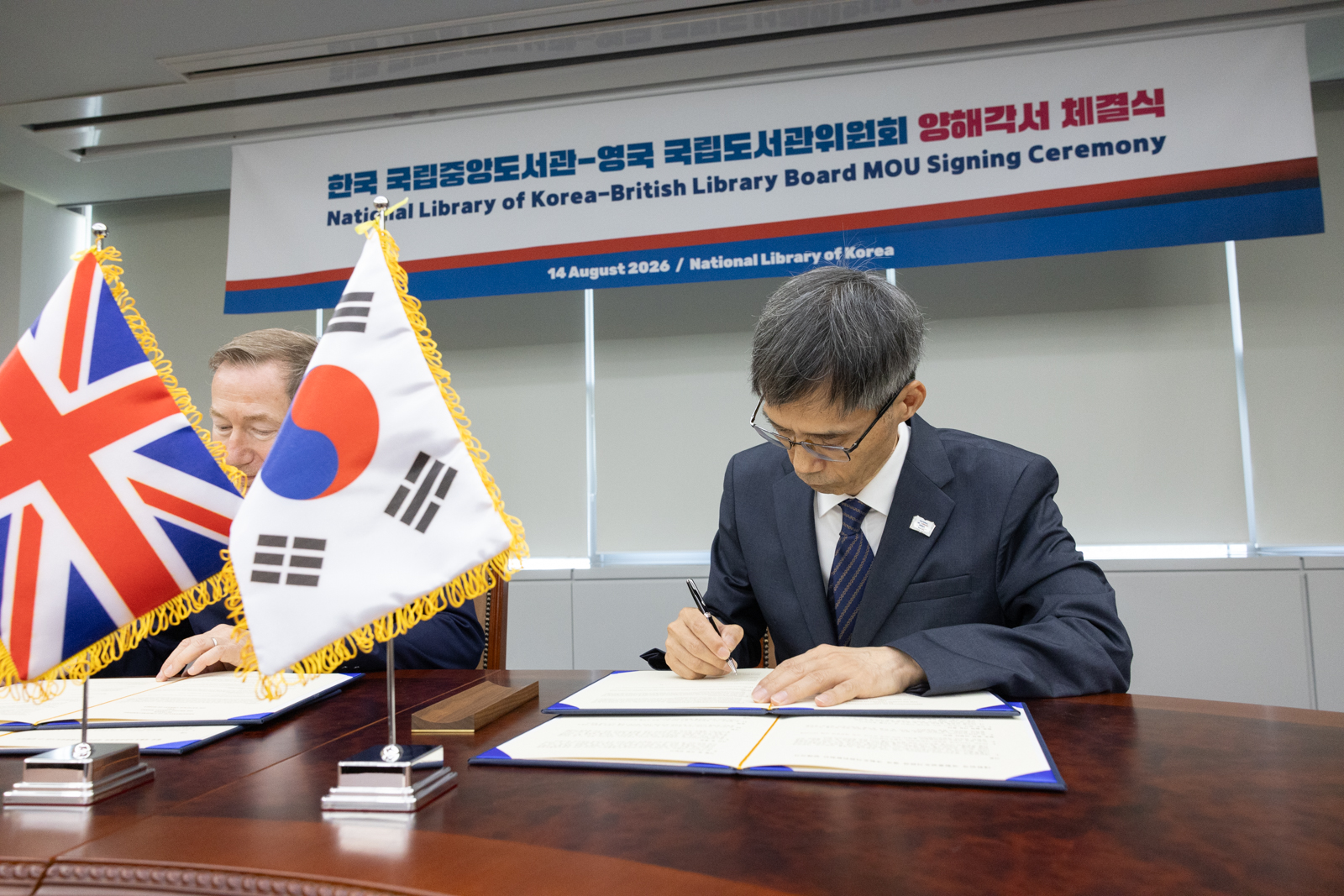 국립중앙도서관 남영준 관장과 영국 국립도서관위원회 영국 국립도서관장 직무대행 제레미 실버 (Jeremy Silver)가 양해각서에 서명을 하고 있는 모습